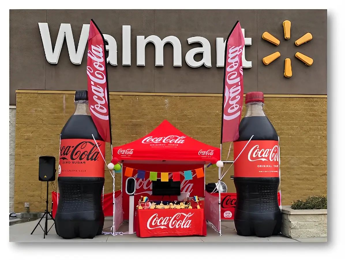 Coca-Cola promotional tent outside a Walmart with large Coke bottle inflatables, flags, and colorful banners.