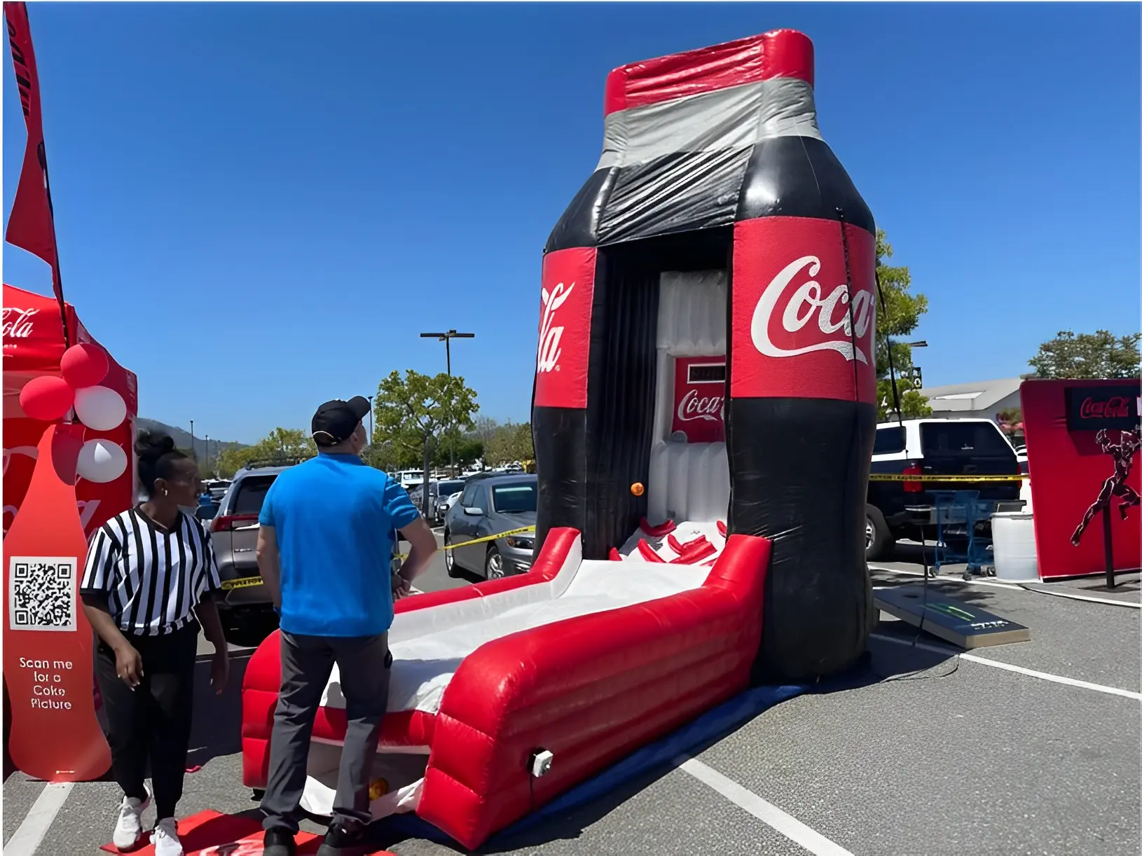 Inflatable Coca-Cola-themed basketball game set up in a parking lot with two people nearby, one appearing to be a referee.
