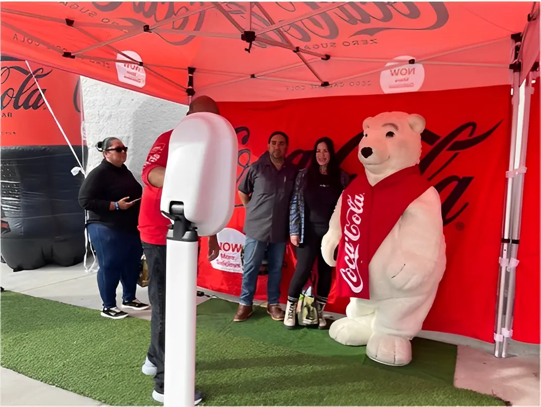 People posing with a person in a Coca-Cola polar bear costume under a red Coca-Cola tent.