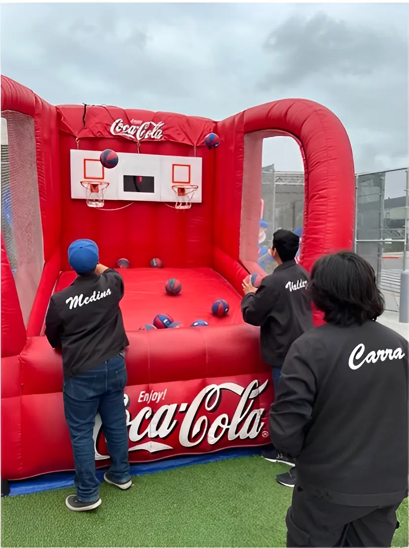 Three people are playing basketball on a red inflatable Coca-Cola-themed hoop game.