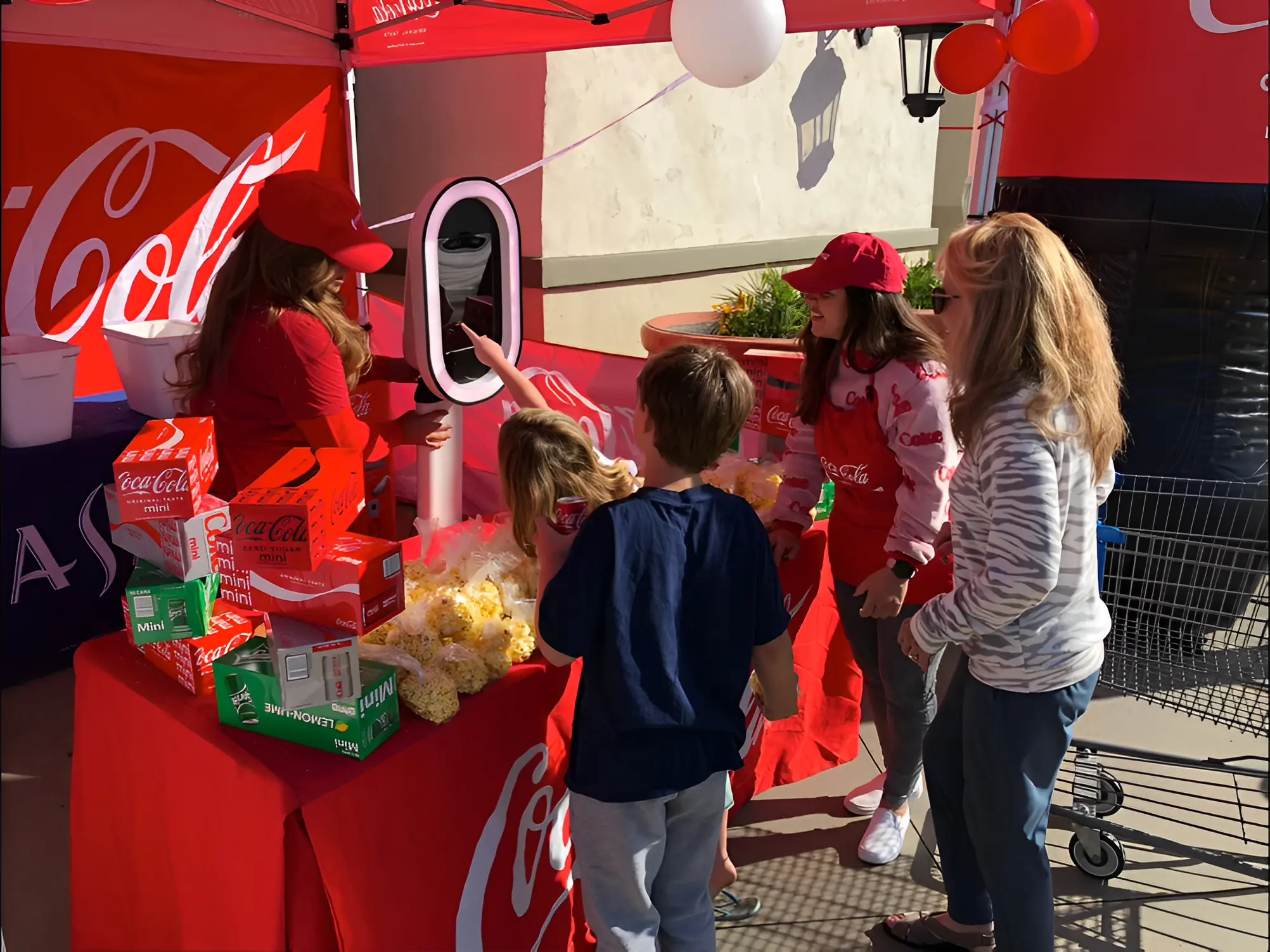 A Coca-Cola promotional booth with staff handing out snacks and drinks to three people, including two children.